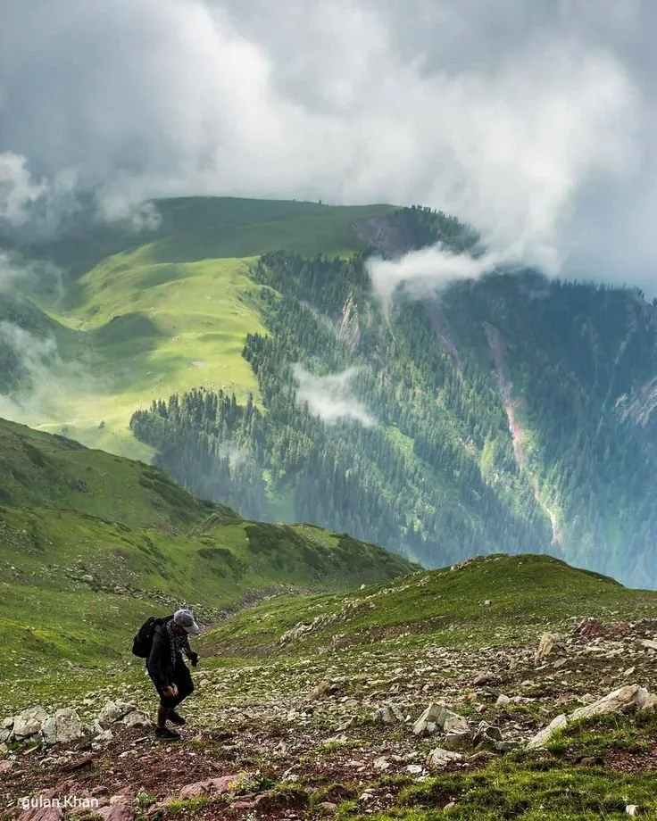 A hiker crossing a rocky ridge above the green valleys of Kaghan